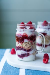 Mason jars filled with berries, granola and yoghurt with a blue background