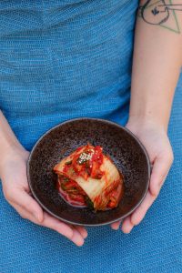 Probiotics. Woman holding bowl of fermented Korean kimchi food wearing blue dress.