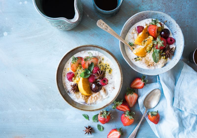 two bowls of yoghurt with fruit and berry toppings on a light blue table