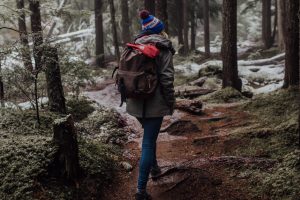 Girl wearing a coat and backpack is hiking in the forest, with her back turned.