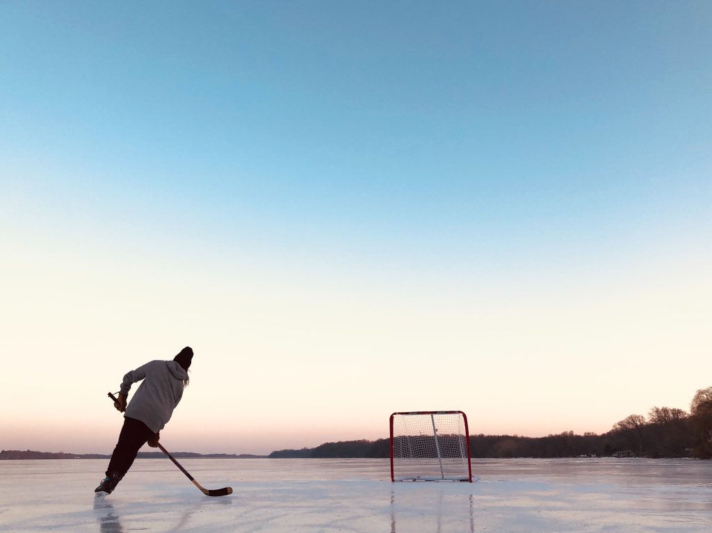 Woman skating on an iced lake with a hockey stick and goal net