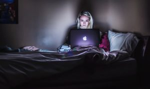 Girl working on her laptop in the dark in her bedroom. 