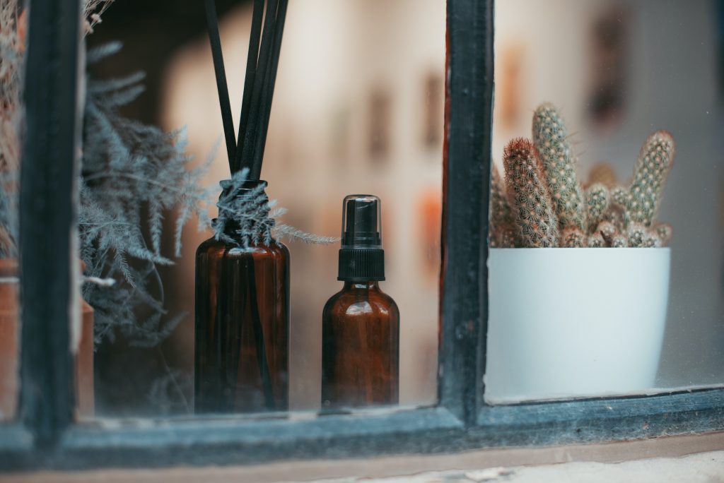 Plants, a spray bottle an an oil diffuser is displayed behind a window pane painted green.