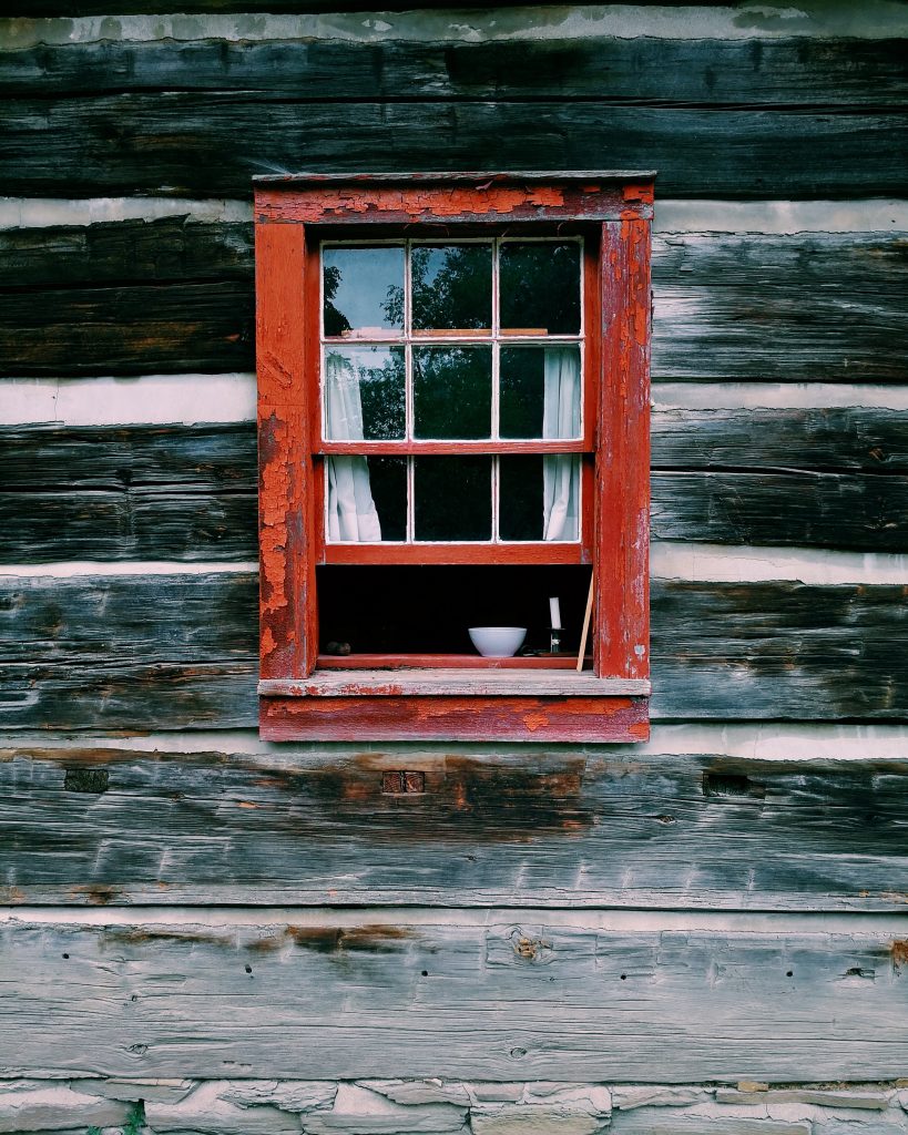 Old window with wooden frame painted red on an exterior wall made of wood panels. The window is open.