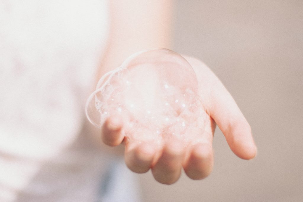 A caucasian hand is reached out and covered in soapy bubbles and suds. 