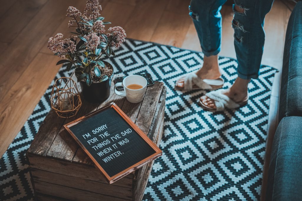 Girl with sandals standing on a blue and white rug with a table and a cup tea. 