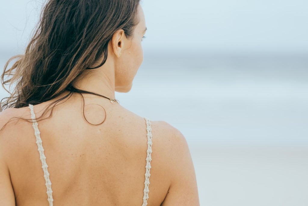 A photo from behind a young woman with long hair looking at the ocean