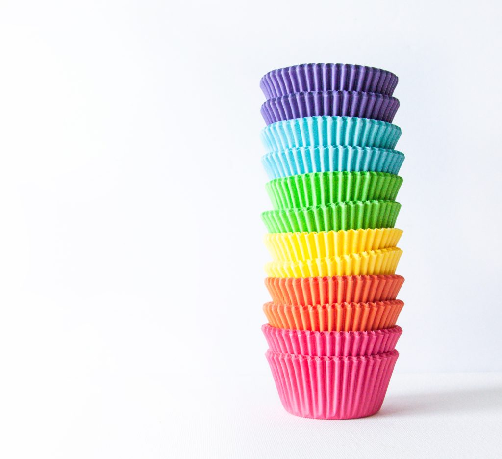 Silicone muffin cups in rainbow colours stacked on top of each other, on a white background.