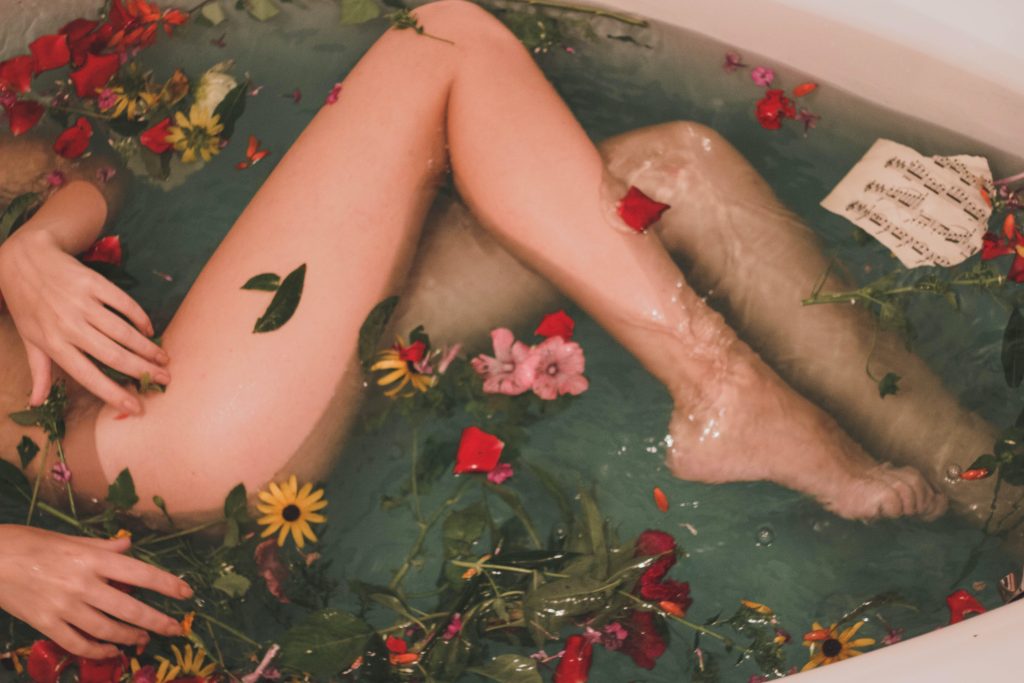 naked woman resting her legs in a bathtub filled with flowers