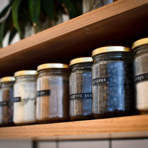 Wooden shelf holding jars filled with spices and herbs.