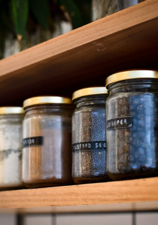 Wooden shelf holding jars filled with spices and herbs.