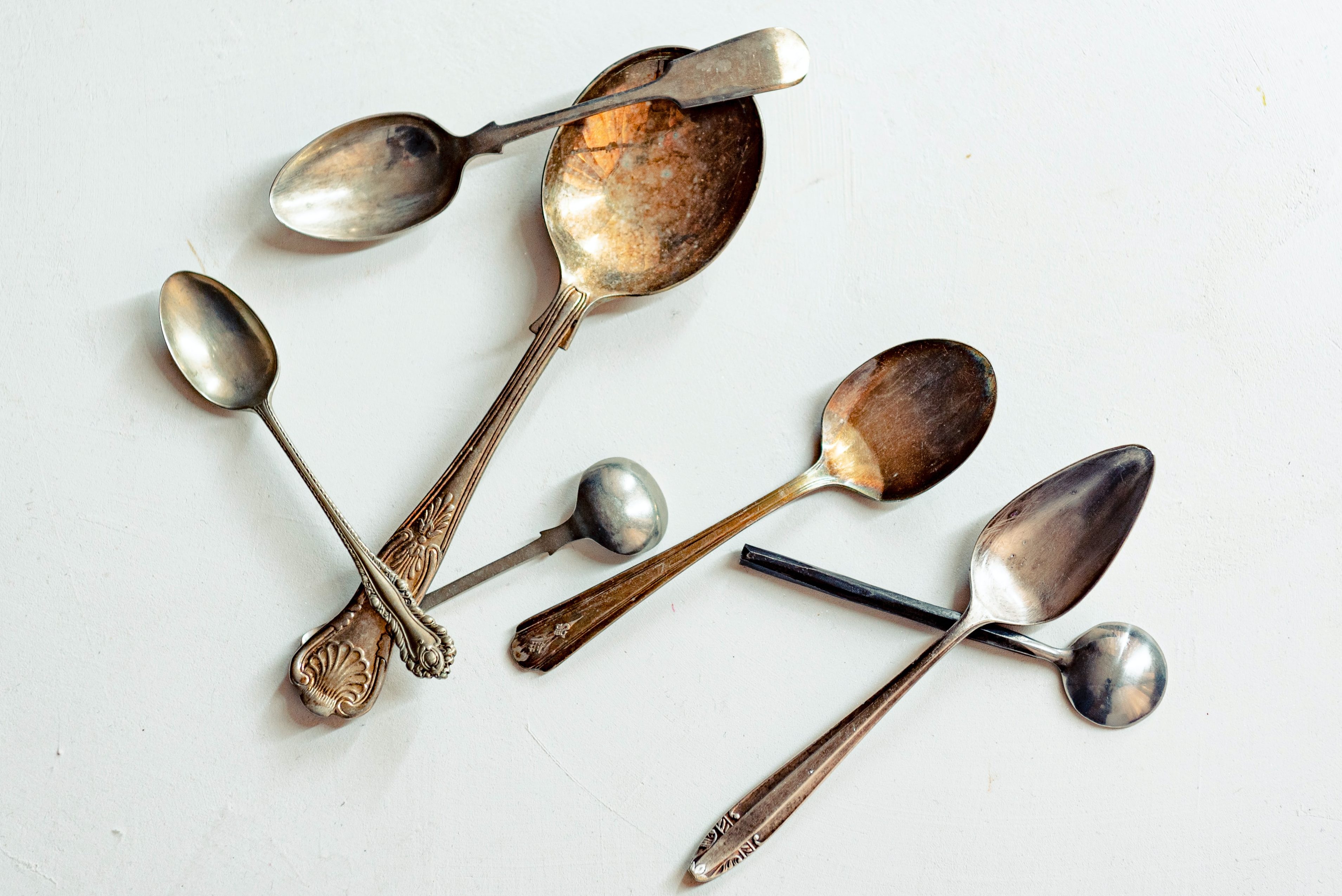 An assortment of silver and bronze spoons of different shapes on a white background.