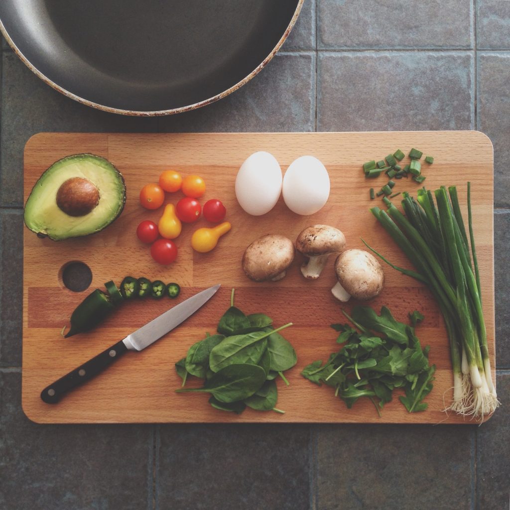 Cutting board with various vegetables and herbs, eggs and a knife on a counter top. 