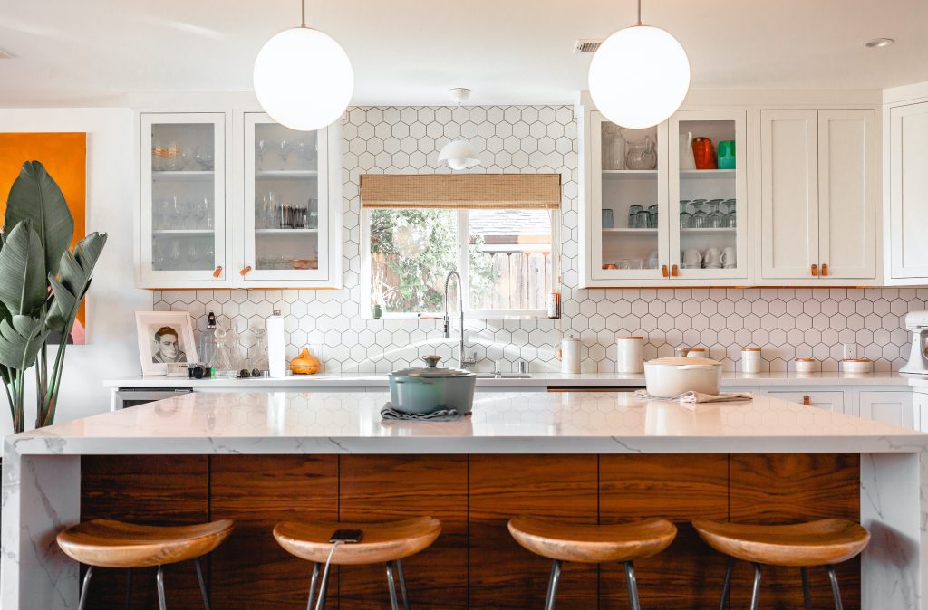 Model kitchen with an island countertop and counter chairs. White cupobards and a white background.