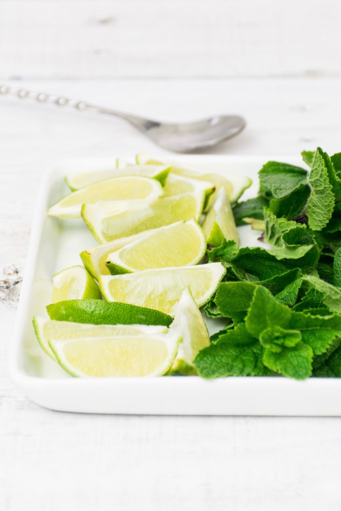 Display of lime wedges and fresh mint on a white ceramic tray on a white marble table